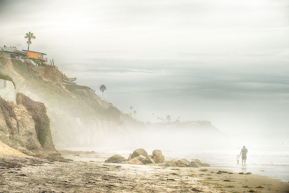 father holding hands with daughter on beach in misty leucadia california