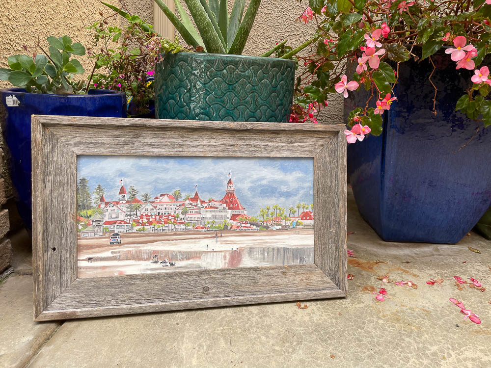 oil painting of hotel del in rustic frame sitting next to flowers
