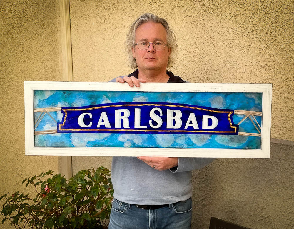 roy holding oil painting of carlsbad sign